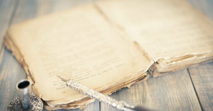 An old and worn out book beside a pen.