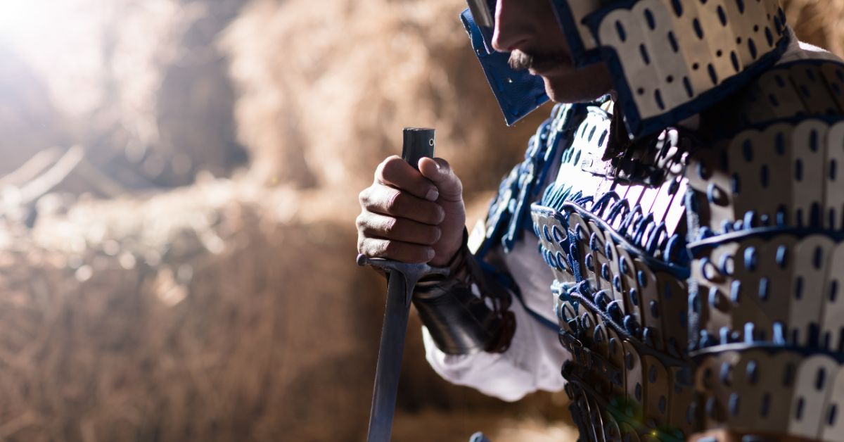 Armored warrior holding a sword while sitting down.