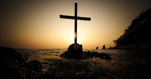 A cross seen in a sea at sunset.