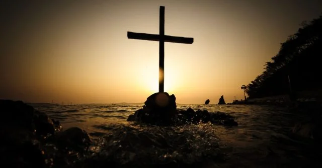 A cross seen in a sea at sunset.