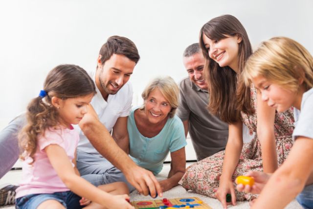 A whole family smiling while playing a board game.