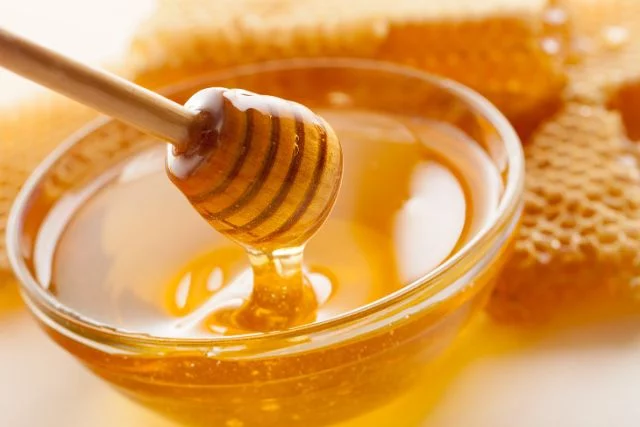 Honey in a bowl with honeycombs at the side.