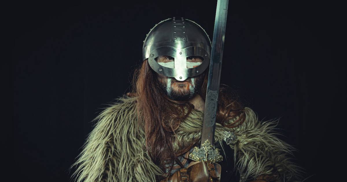 A viking with long brown hair holding a sword.