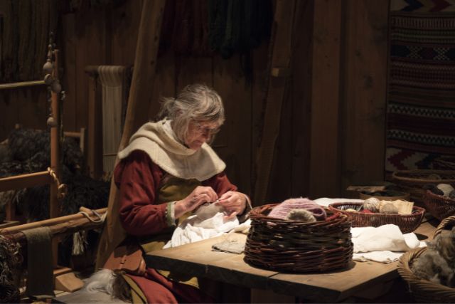 An old viking woman sewing clothes for her family.