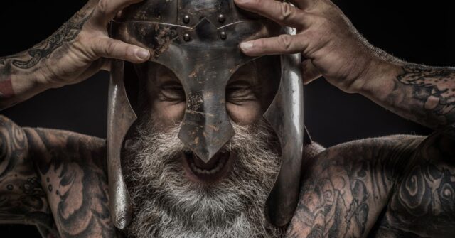 Bearded viking with tattoos wearing a helmet.