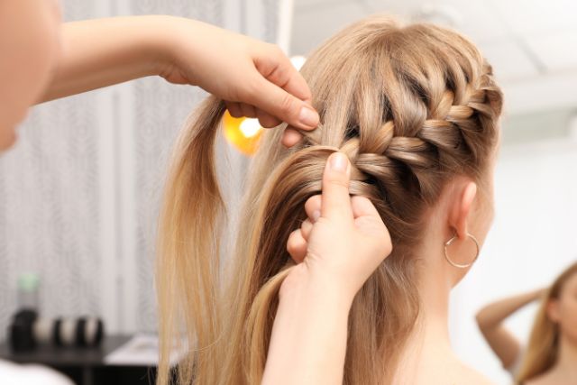 A hairstylist doing a classic braid on blonde hair.