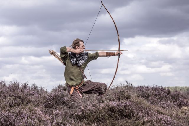A viking warrior using bow and arrow outside.