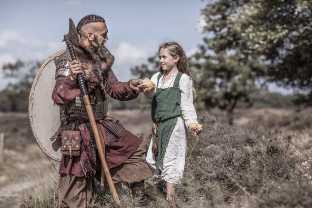 A viking warrior with braided hair talking to a child.