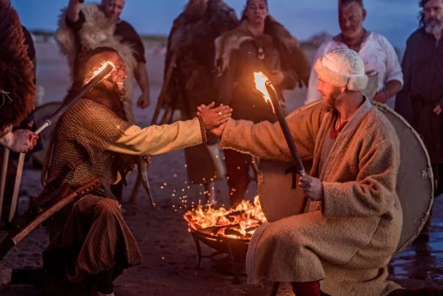 A hoard of viking men gathered around a campfire.