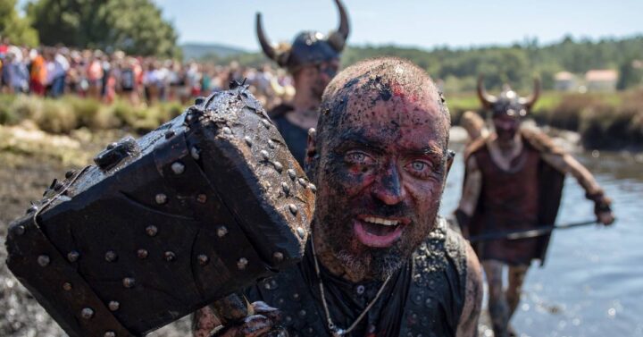 Men in viking costumes running in mud on one of the festival event.