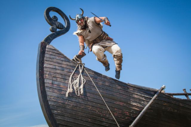 A viking with horned helmet getting off a ship.