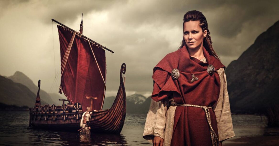A woman viking warrior wearing traditional clothes while standing near a boat.