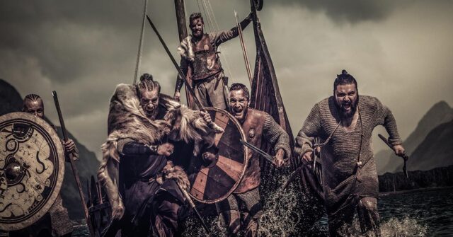 Group of Viking warriors with shield and weapons running towards the enemy from their long boat