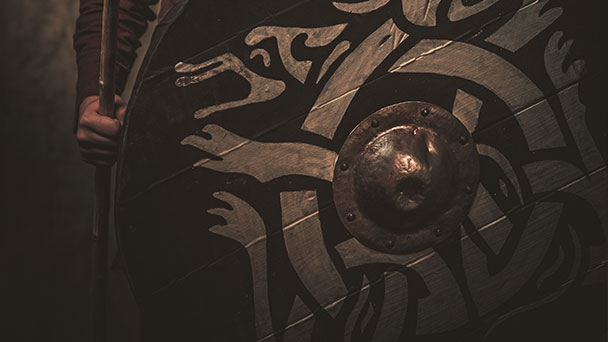 Close up of the front of a Viking shield showing the boss and patterns on the wood.