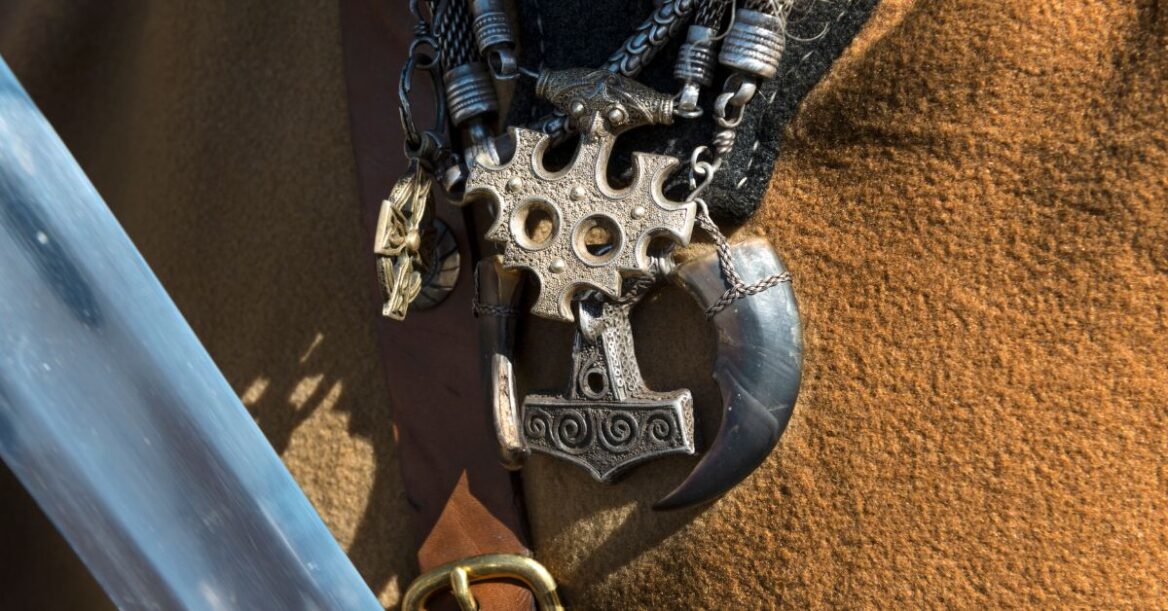 Close up of some necklaces around a Viking with various symbols including Thor's hammer, a horn, cross, etc.