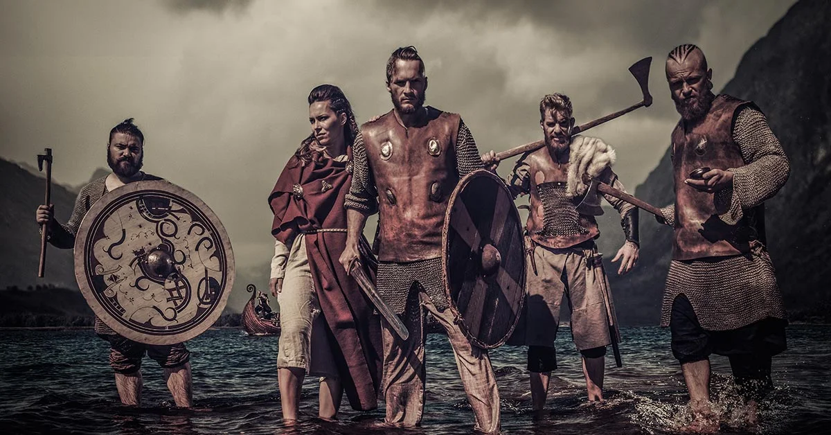 Group of male and female Vikings with weapons, standing in water