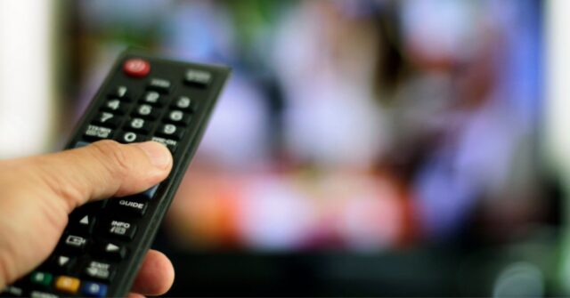 Person holding a Television remote control pointed at the TV.