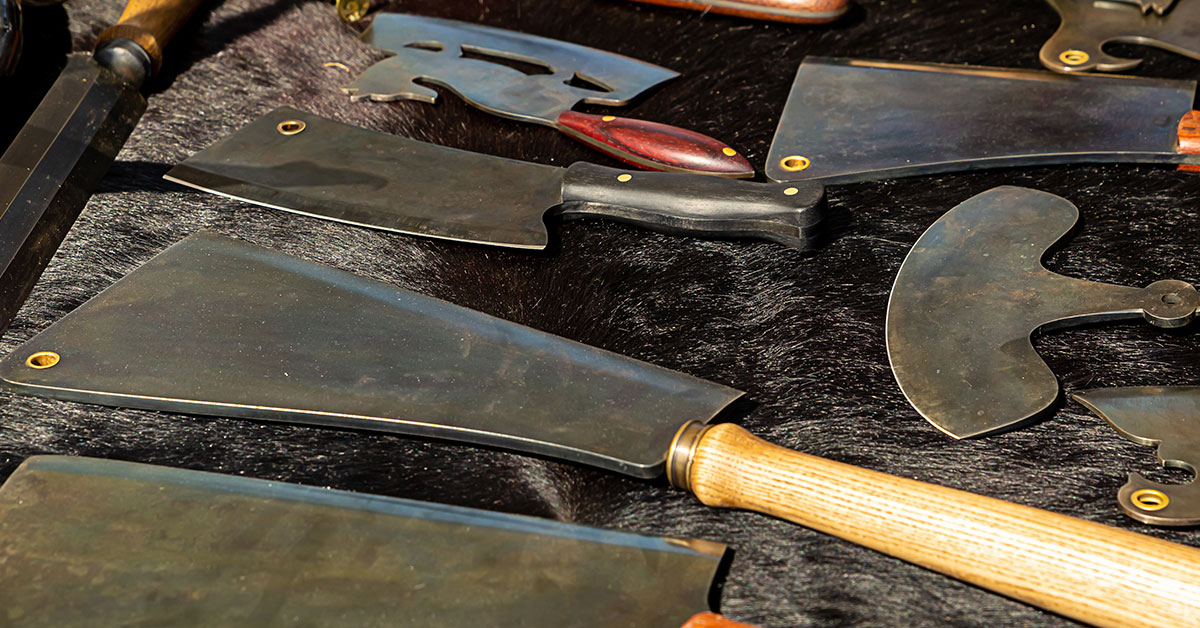 Cutting tools consisting of large blades, knives and axes heads laying down on a black cloth ready for sale.