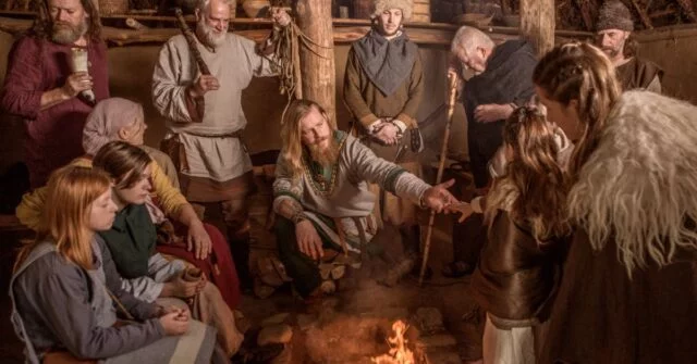 A group of 12 people including a family sitting and standing around an indoor fire to keep warm.