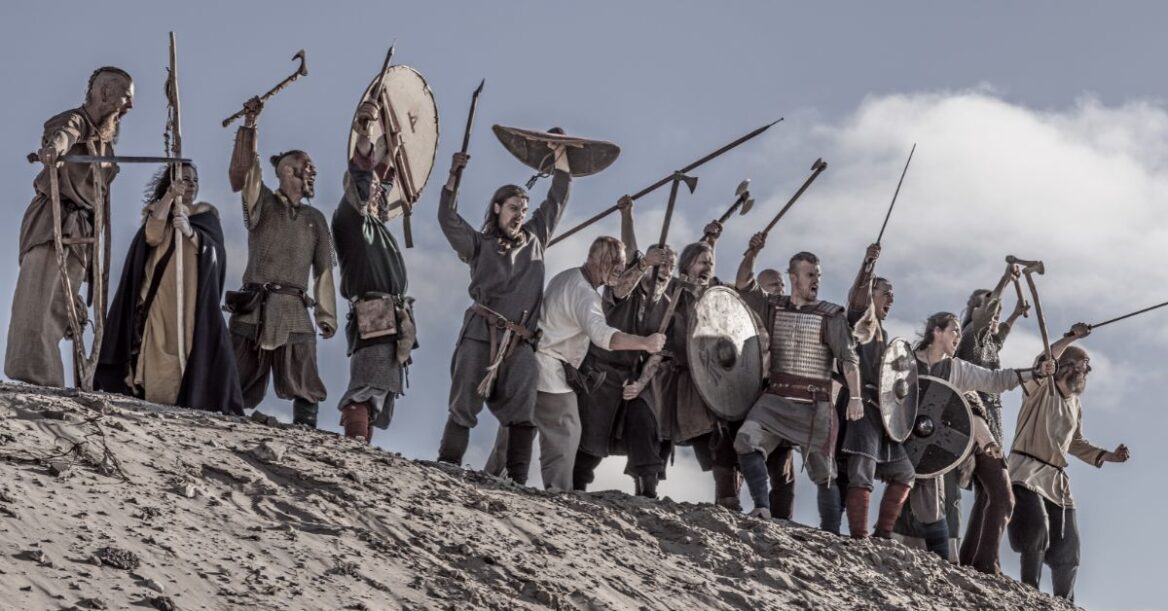 Group of Viking warriors standing on a hill holding their weapons in the air, ready to attack.