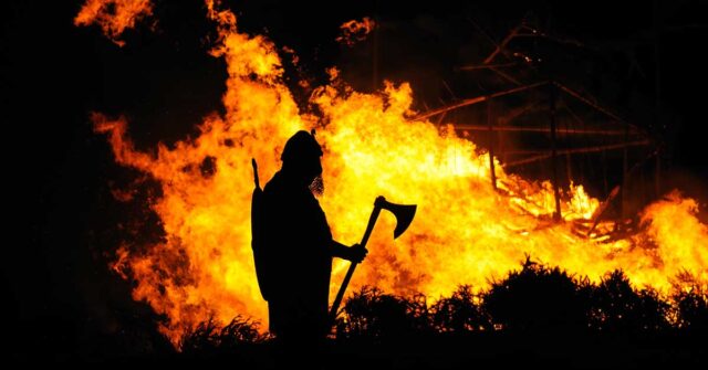 Silhouette of Viking warrior holding an axe with fire burning in the background