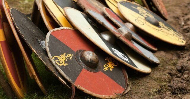 A selection of various traditional Viking shields on the ground stacked next to each other.