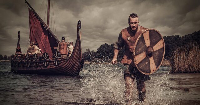 Viking warrior holding a shield and sword running through the water after departing his long boat